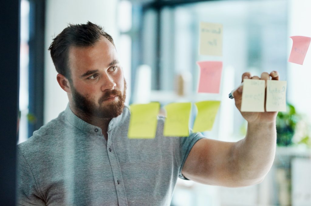 Shot of a young businessman brainstorming with notes on a glass wall in an office